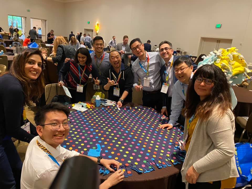 A group of colleagues enjoys the team building experience at the Hope for the Holidays event, working together to assemble colorful blankets for donation to local seniors during the holiday season.