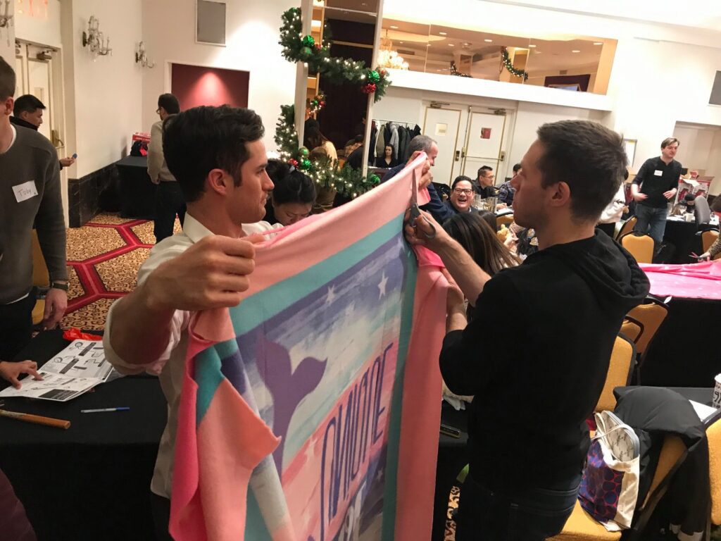 Two team members work together to prepare a fleece blanket during a holiday-themed team building event, contributing to gifts for seniors as part of the Hope for the Holidays program.