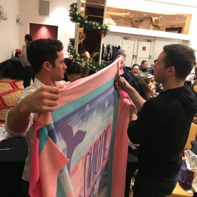 Two team members work together to prepare a fleece blanket during a holiday-themed team building event, contributing to gifts for seniors as part of the Hope for the Holidays program.