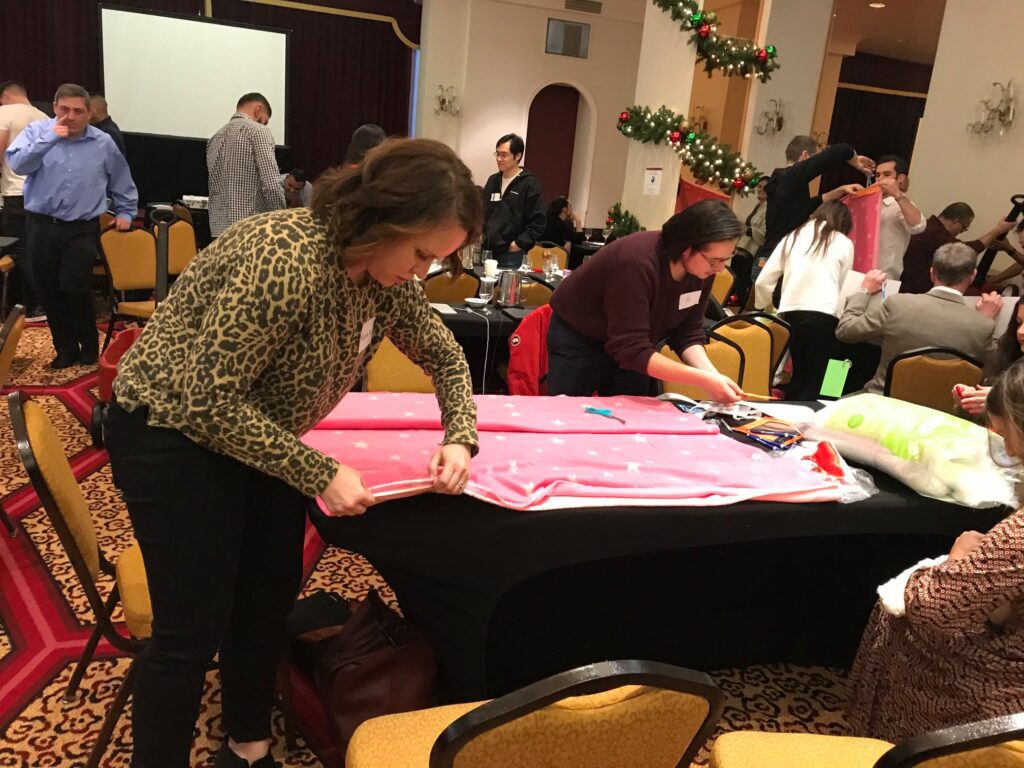 Participants at the Hope for the Holidays team building event work together to craft personalized blankets, spreading warmth and cheer to local seniors during the festive season.