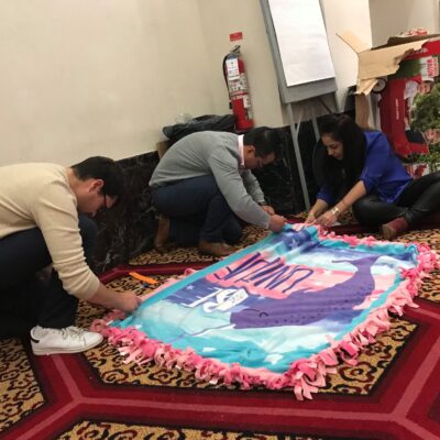 Team members collaborate during the Hope for the Holidays event, carefully crafting a fleece blanket to donate to local seniors as part of their charitable efforts.