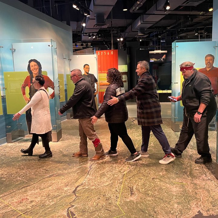 Participants navigating an interactive museum exhibit during a scavenger hunt. The team works together, collaborating to solve clues and explore the museum, enhancing teamwork and problem-solving skills.