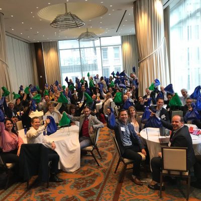 Team members posing with colorful bags during the Team Disaster Relief event. Participants work together to assemble disaster relief care kits, bonding over fun challenges that foster teamwork and communication.